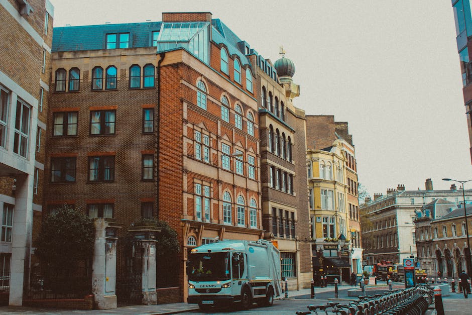 A red double-decker bus displaying the route number 24 and destination 'Hampstead Heath' is stationary on a city street with a clear view of historic buildings and the iconic Tower of London in the ba