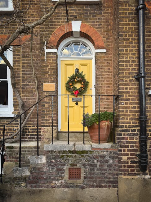 Photograph of the front entrance to a residential property with a yellow door decorated with a Christmas wreath, featuring evergreen branches and red ornaments. The door is set within a brick façade