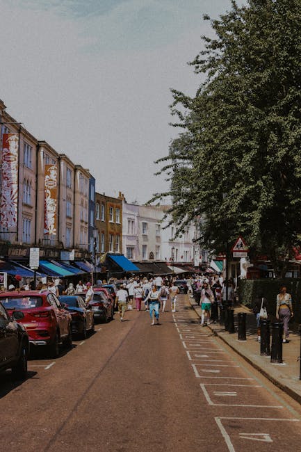 A busy street scene in West Hampstead featuring a row of multi-story buildings with shops on the ground level and residential apartments above. The buildings are constructed with brick and white facad